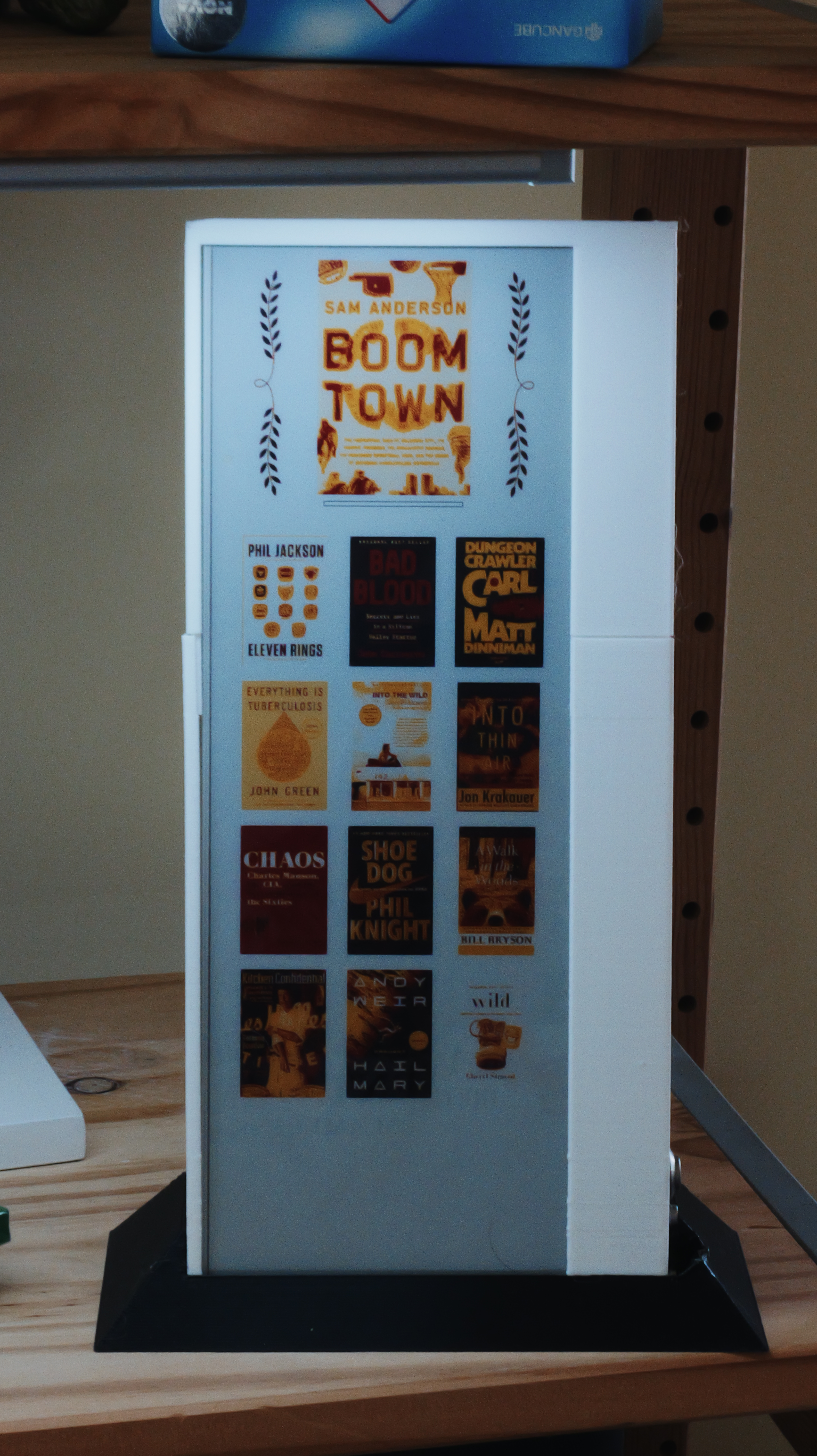 A framed color e-ink display showing book covers on a wooden bookshelf