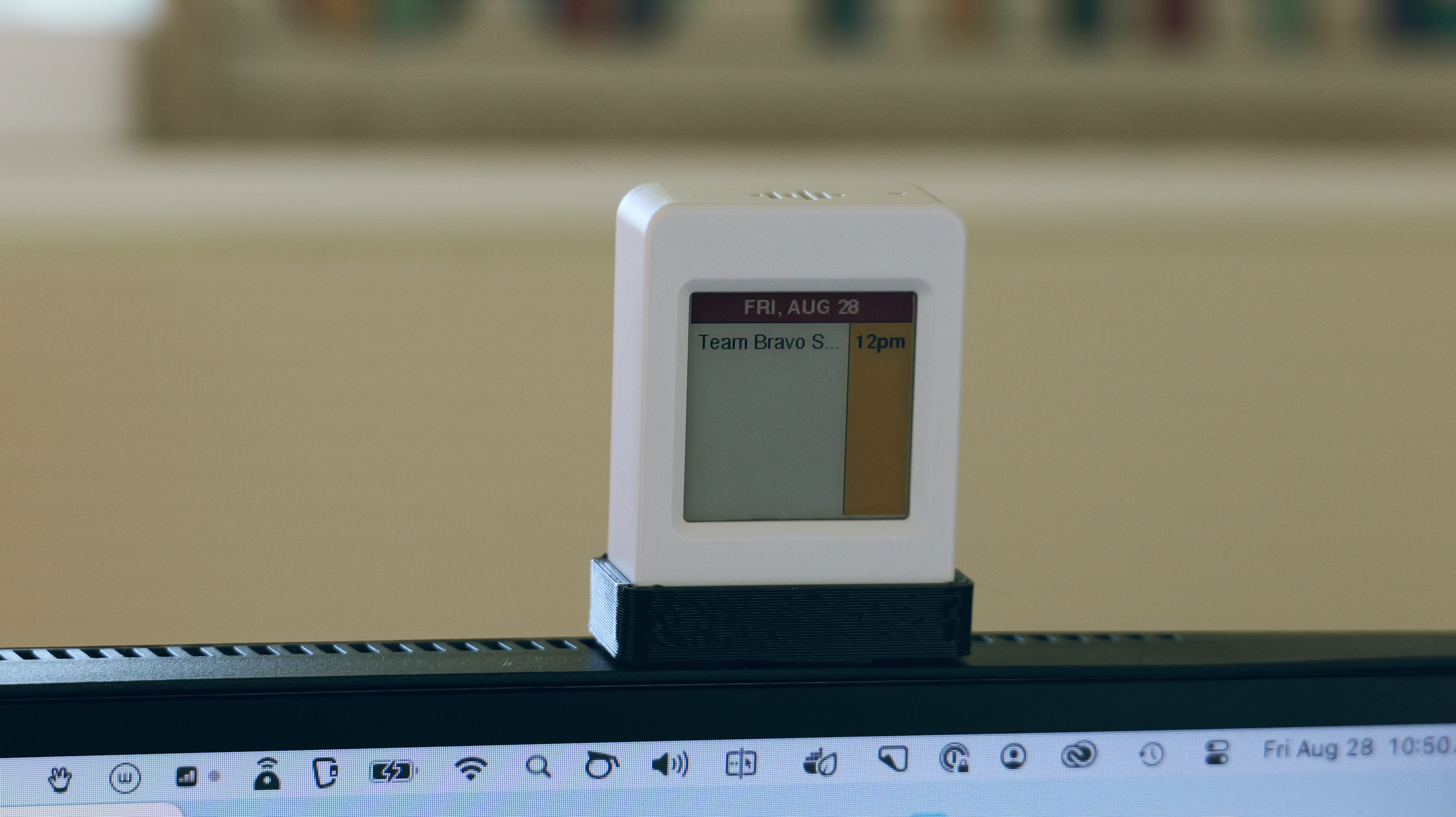 A small white e-ink meeting display in a black stand on top of a monitor